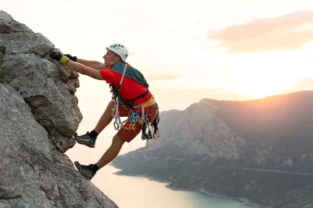 Jovem alpinista masculino escala uma rota difícil com vista para o mar ao pôr do sol