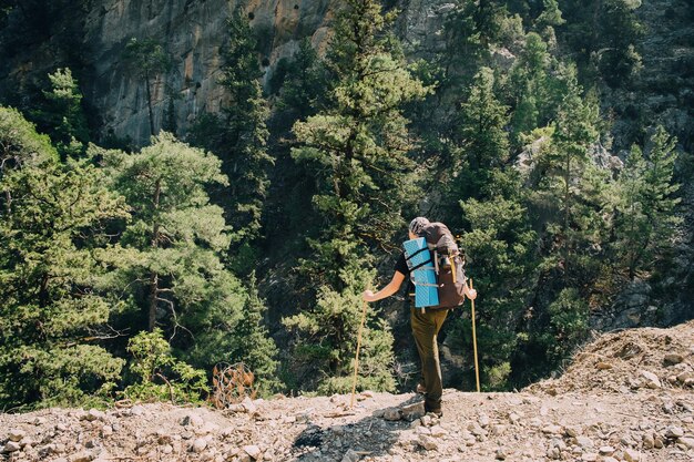 Jovem alpinista masculino esportivo, caminhadas com mochila nas montanhas, floresta escura com grandes pinheiros. esporte e conceito de vida ativa.