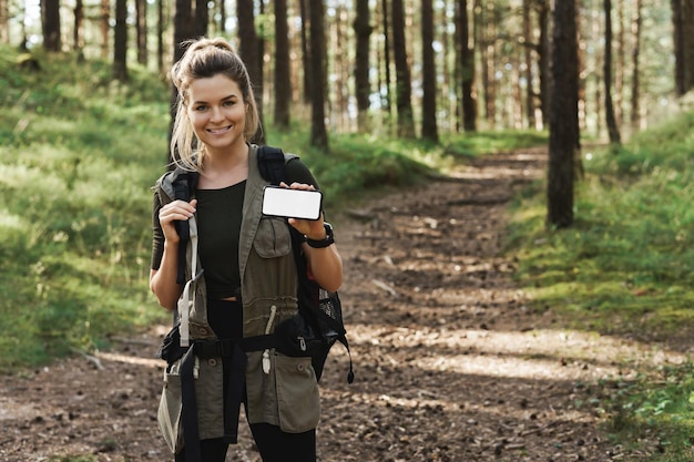 Jovem alpinista mostrando smartphone com tela em branco em floresta verde