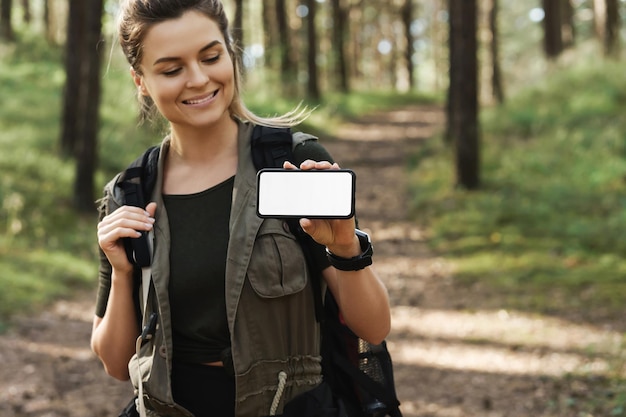 Foto jovem alpinista mostrando smartphone com tela em branco em floresta verde