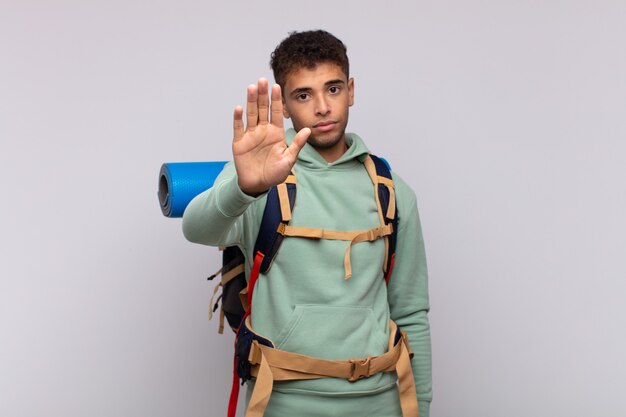 Jovem alpinista parecendo sério, severo, descontente e irritado, mostrando a palma da mão aberta fazendo gesto de pare