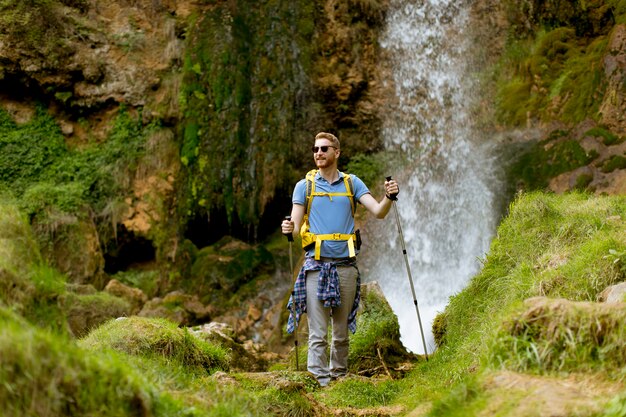 Jovem alpinista parou ao lado de uma cachoeira da montanha para descansar