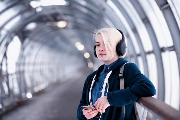 Jovem aluna ouvindo música em grandes fones de ouvido no túnel do metrô