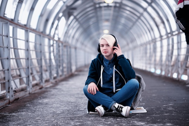 Jovem aluna ouvindo música em grandes fones de ouvido no túnel do metrô