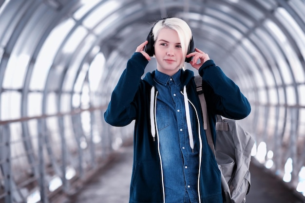 Jovem aluna ouvindo música em grandes fones de ouvido no túnel do metrô