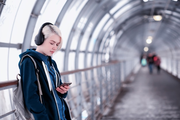 Jovem aluna ouvindo música em grandes fones de ouvido no túnel do metrô