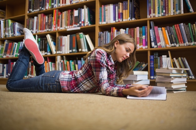 Jovem aluno deitado na leitura do chão da biblioteca