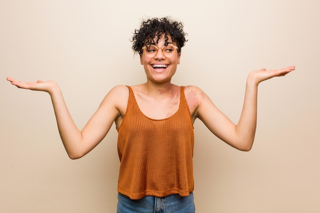 Foto jovem americana africano com marca de nascimento de pele faz escala com os braços, sente-se feliz e confiante.