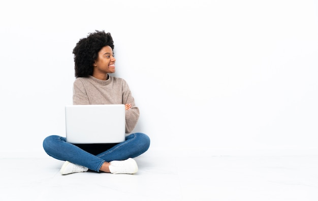 Jovem americana Africano com um laptop sentado no chão em posição lateral