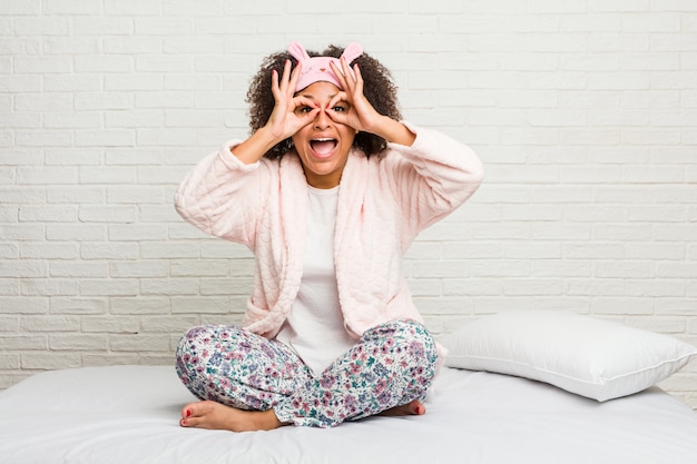 Jovem americana africano na cama vestindo pijama mostrando sinal bem sobre os olhos