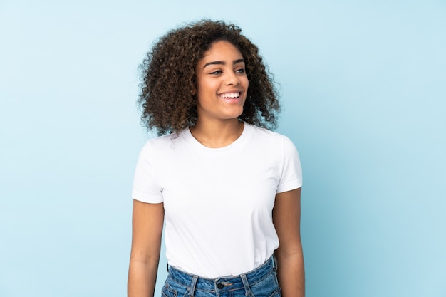 Jovem americana Africano na parede azul, olhando para o lado e sorrindo