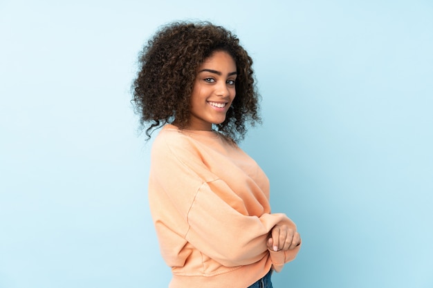 Jovem americana Africano na parede azul, olhando para o lado e sorrindo