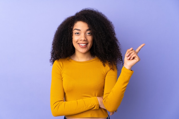 Jovem americana Africano na parede roxa feliz e apontando para cima