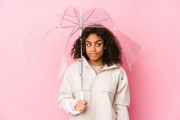 Jovem americana Africano segurando um guarda-chuva confuso, sente-se duvidoso e inseguro.