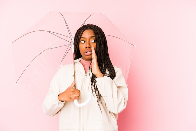 Jovem americana Africano segurando um guarda-chuva está dizendo um segredo e olhando de lado