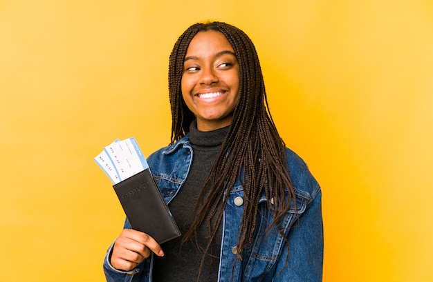 Jovem americana Africano segurando um passaporte olha de lado sorrindo, alegre e agradável.