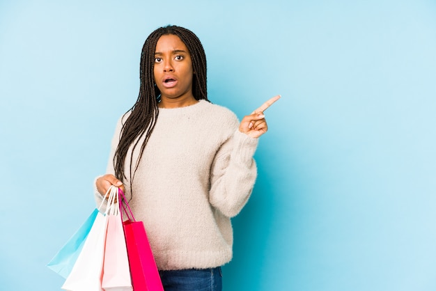 Jovem americana Africano segurando uma sacola de compras isolada apontando para o lado