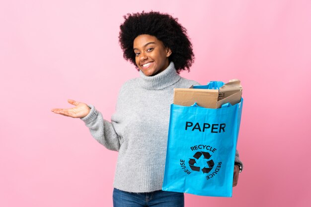 Jovem americana Africano segurando uma sacola de reciclagem na parede colorida, apresentando uma idéia enquanto olha sorrindo para