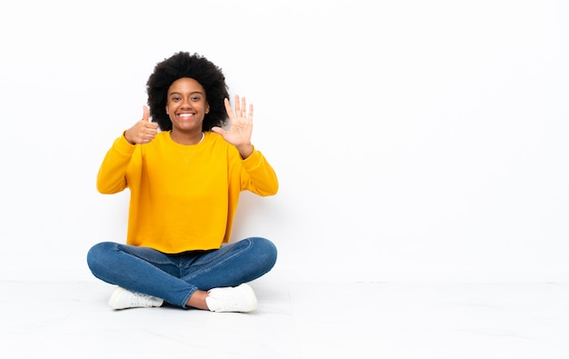 Jovem americana africano, sentada no chão, contando seis com os dedos