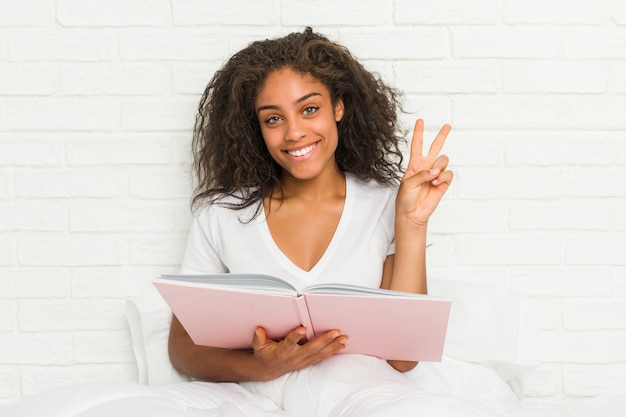 Jovem americana africano sentado na cama estudando mostrando o número dois com os dedos.