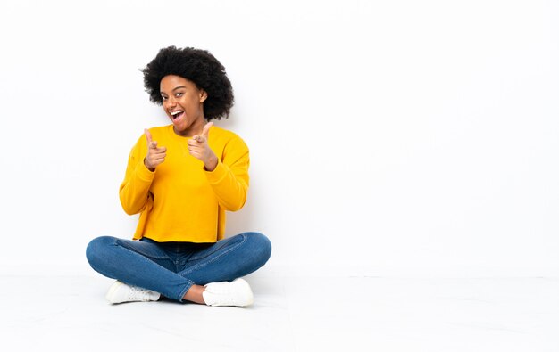 Jovem americana Africano sentado no chão apontando para a frente e sorrindo