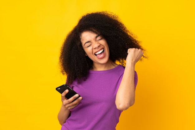 Jovem americana Africano sobre parede com telefone em posição de vitória