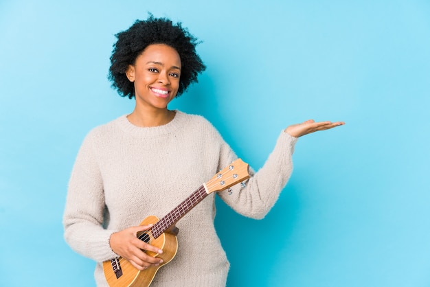 Jovem americana africano tocando ukelele mostrando um espaço em branco na palma da mão e segurando a guitarra