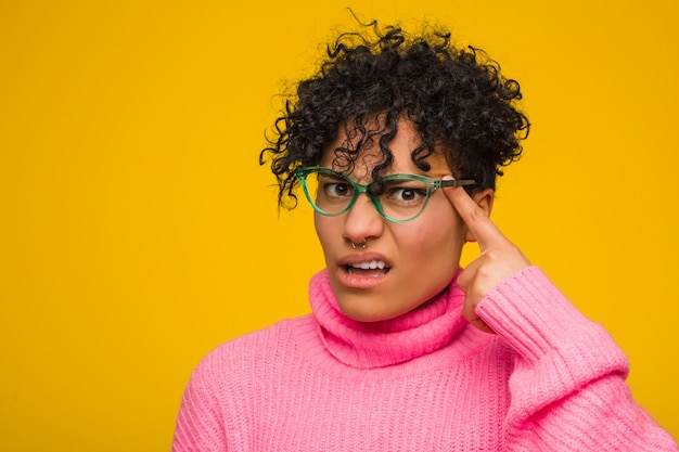 Jovem americana Africano vestindo uma blusa rosa, mostrando um gesto de decepção com o dedo indicador.