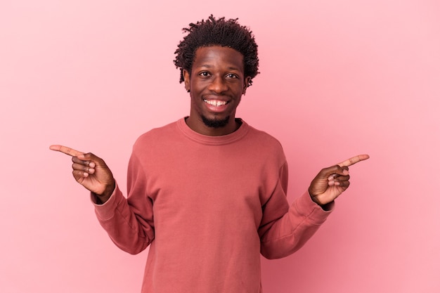 Jovem americano africano isolado em um fundo rosa apontando para diferentes espaços de cópia, escolhendo um deles, mostrando com o dedo.