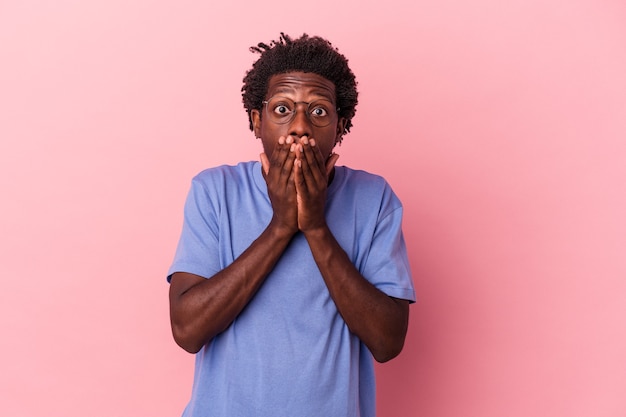 Jovem americano africano isolado em um fundo rosa chocado, cobrindo a boca com as mãos.