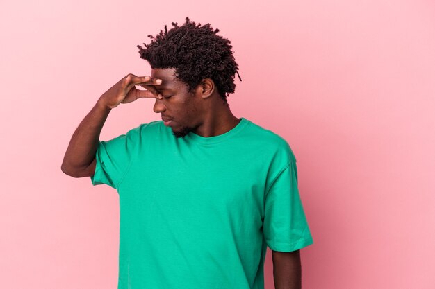 Jovem americano africano isolado em um fundo rosa, tendo uma dor de cabeça, tocando a frente do rosto.