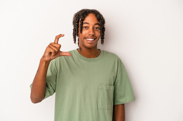 Jovem americano africano isolado no fundo branco, segurando algo pequeno com os indicadores, sorrindo e confiante.