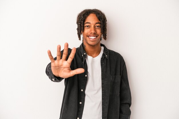 Jovem americano africano isolado no fundo branco, sorrindo alegre mostrando o número cinco com os dedos.