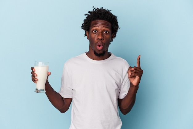 Jovem americano africano segurando um copo de leite isolado sobre fundo azul, tendo uma ótima ideia, o conceito de criatividade.