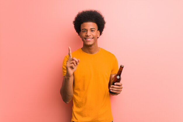 Jovem americano africano segurando uma cerveja, mostrando o número um