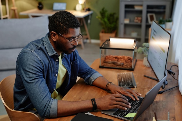 Jovem analista ocupado ou corretor digitando no teclado do laptop no local de trabalho