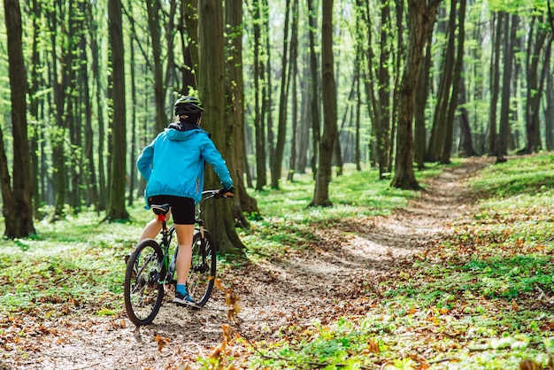 Jovem anda de bicicleta na floresta por trilha