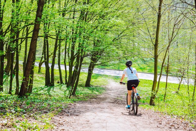 Jovem anda de bicicleta na floresta por trilha