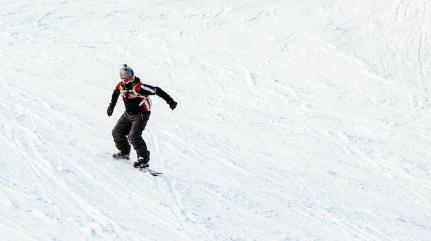 Jovem anda de snowboard nas encostas das montanhas.