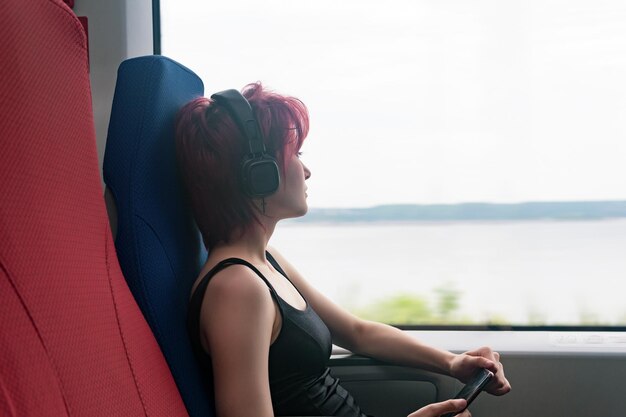 Jovem anda de trem ouvindo música e olhando pela janela