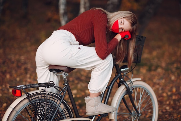 Jovem andando de bicicleta em luvas vermelhas e máscara facial no parque outono