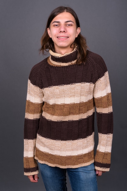 Foto jovem andrógino bonito com cabelo comprido pronto para o inverno contra uma parede cinza