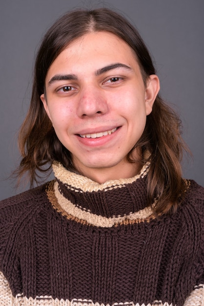 jovem andrógino bonito com cabelo comprido pronto para o inverno contra uma parede cinza