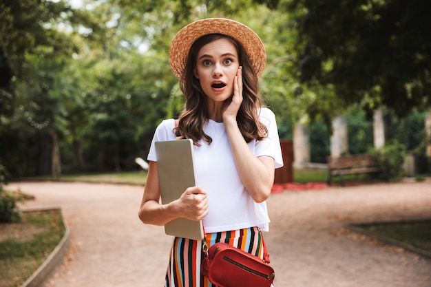 Jovem animada sentada com um laptop no parque ao ar livre