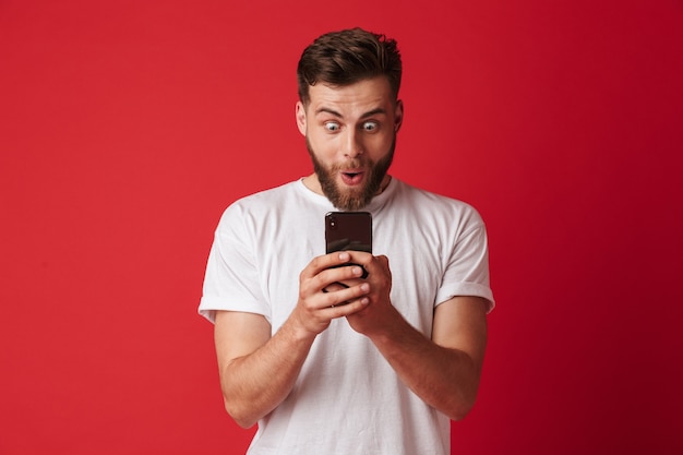 Jovem animado chocado usando telefone celular.