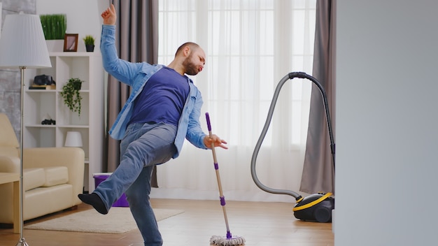 Jovem animado dançando enquanto limpa seu apartamento