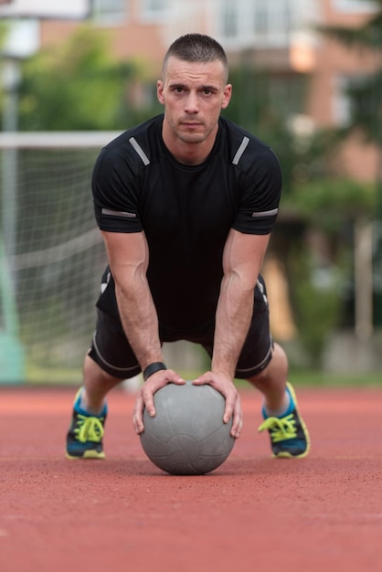 Jovem ao ar livre realizando flexões no exercício de musculação com bola medicinal