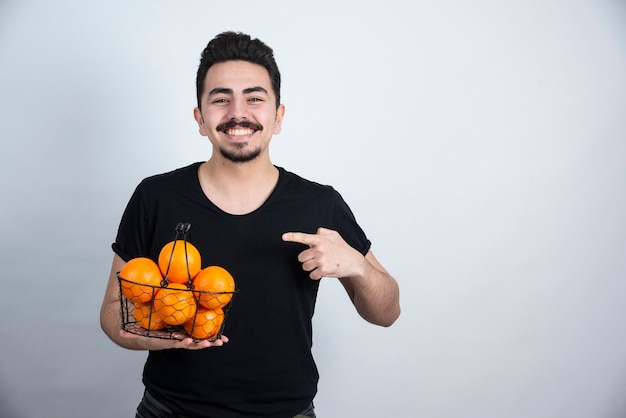 Jovem apontando para a cesta metálica cheia de frutas laranja.