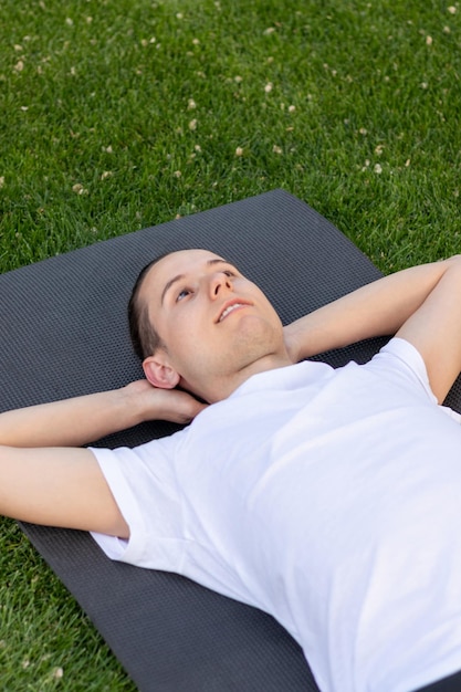 Jovem aproveitando o tempo de descanso no jardim olhando para o céu claro em uma camiseta branca no parque