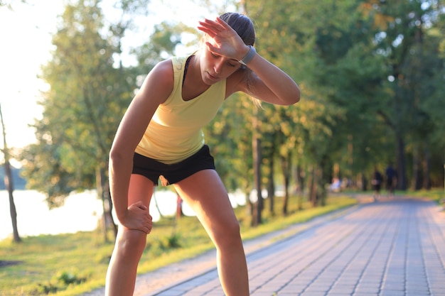 Jovem aptidão atraente garota esportiva descansando após noite intensiva correr ao ar livre ao pôr do sol no parque.